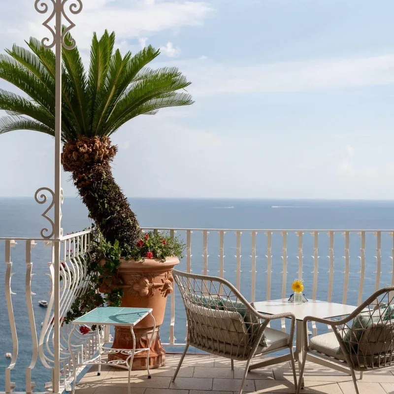 Seaside balcony with table, chairs and a potted palm.