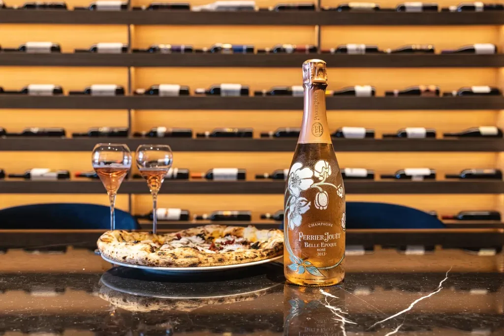 Sparkling wine and glasses beside a wine rack.