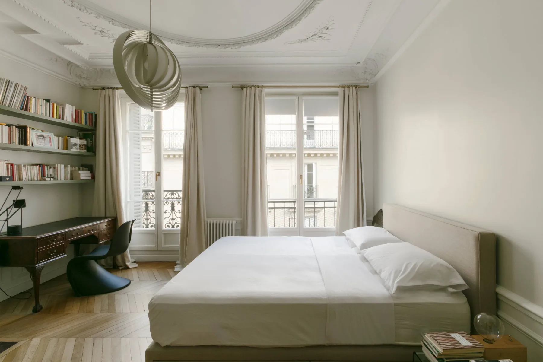 Dormitorio con una cama bien tendida, ventanas altas y estanterías empotradas.