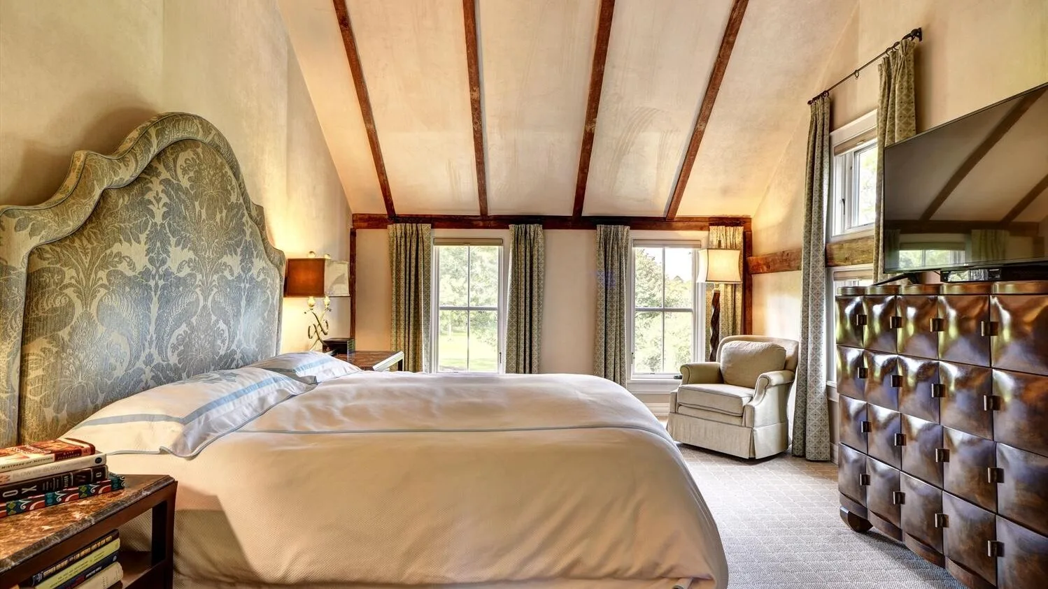 A bedroom with a large bed, two windows, and a tufted dresser.