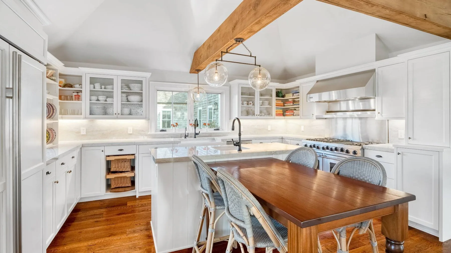 A bright kitchen with white cabinets, a wood dining table, and exposed ceiling beams.