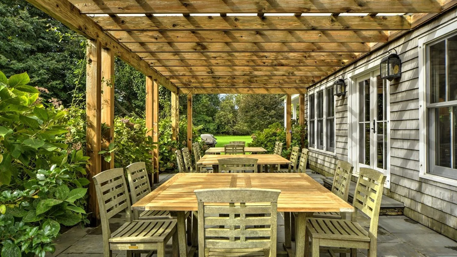 A covered outdoor dining area with a wooden table and seating beside the house.