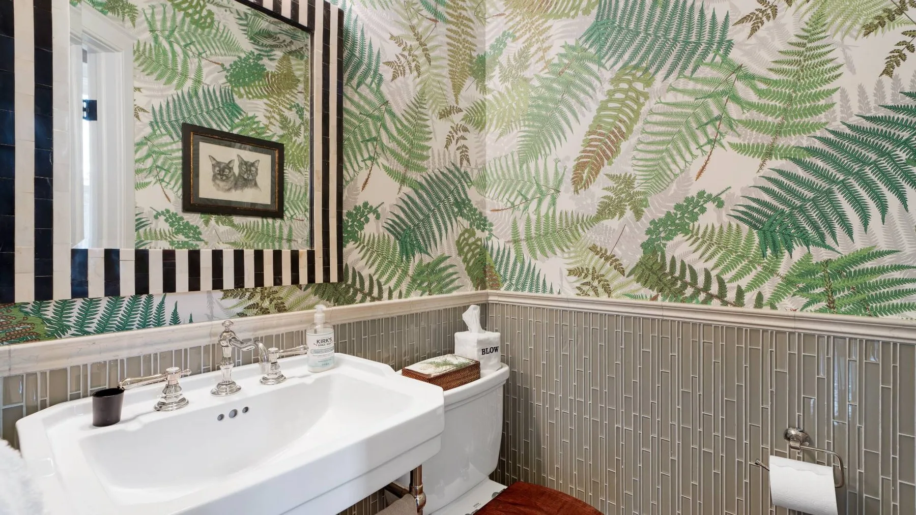 A bathroom with a white sink, toilet, and fern-patterned wallpaper.