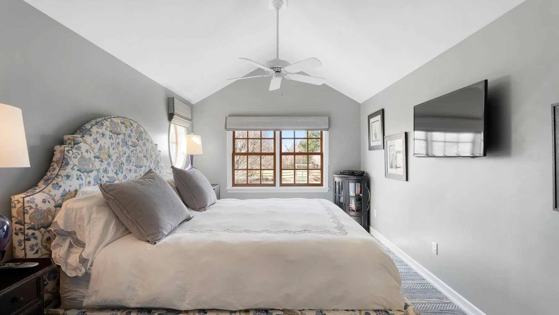 A bedroom with a large bed, patterned headboard, and window.