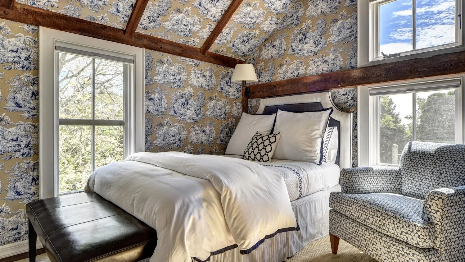 A bedroom with a bed, patterned walls, and a window overlooking trees.