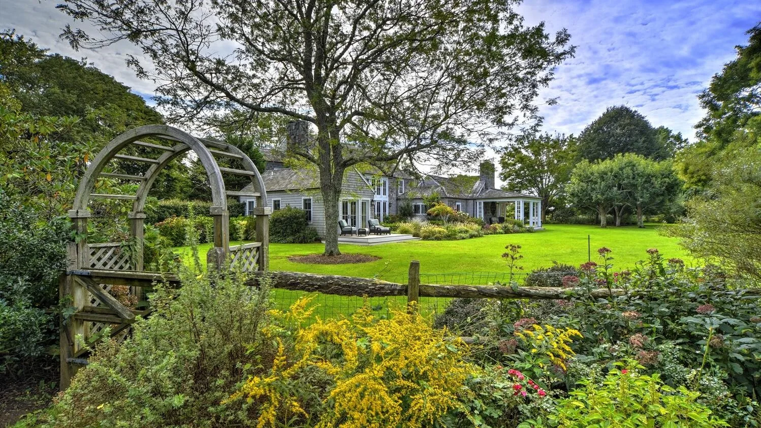 A landscaped garden with a broad lawn, flower beds, and a house in the background.