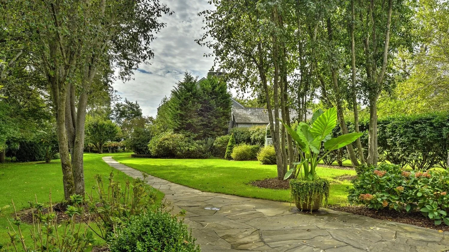 A landscaped garden with a stone path winding through green lawns and trees.