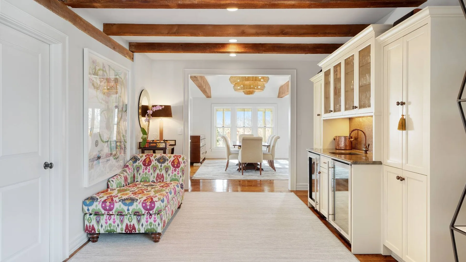 A bright open-plan kitchen and sitting area with colorful seating and white cabinetry.