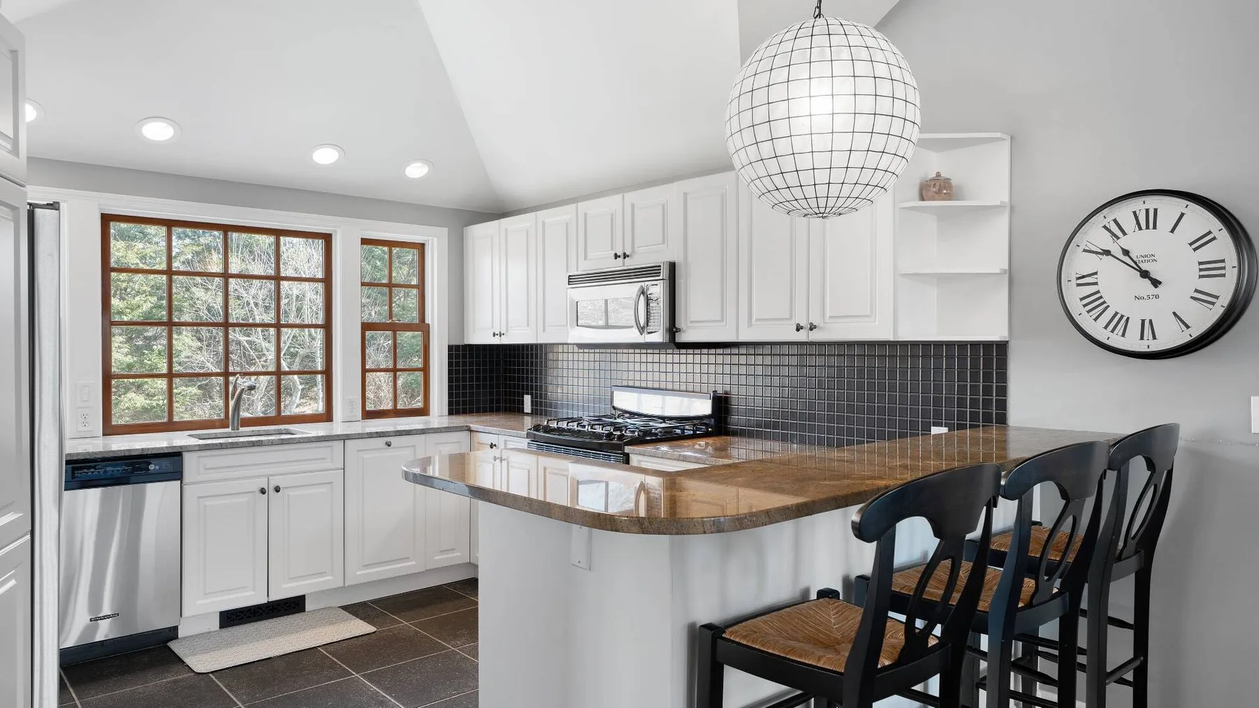 A bright kitchen with white cabinets, a central counter, and bar seating.