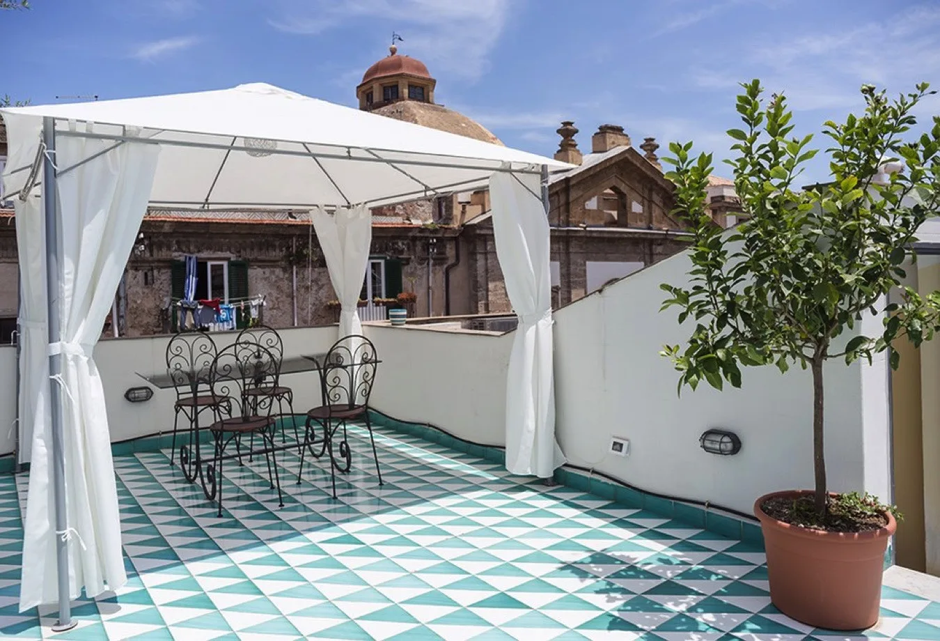 Una terraza exterior embaldosada tiene un toldo, asientos y un árbol en maceta.