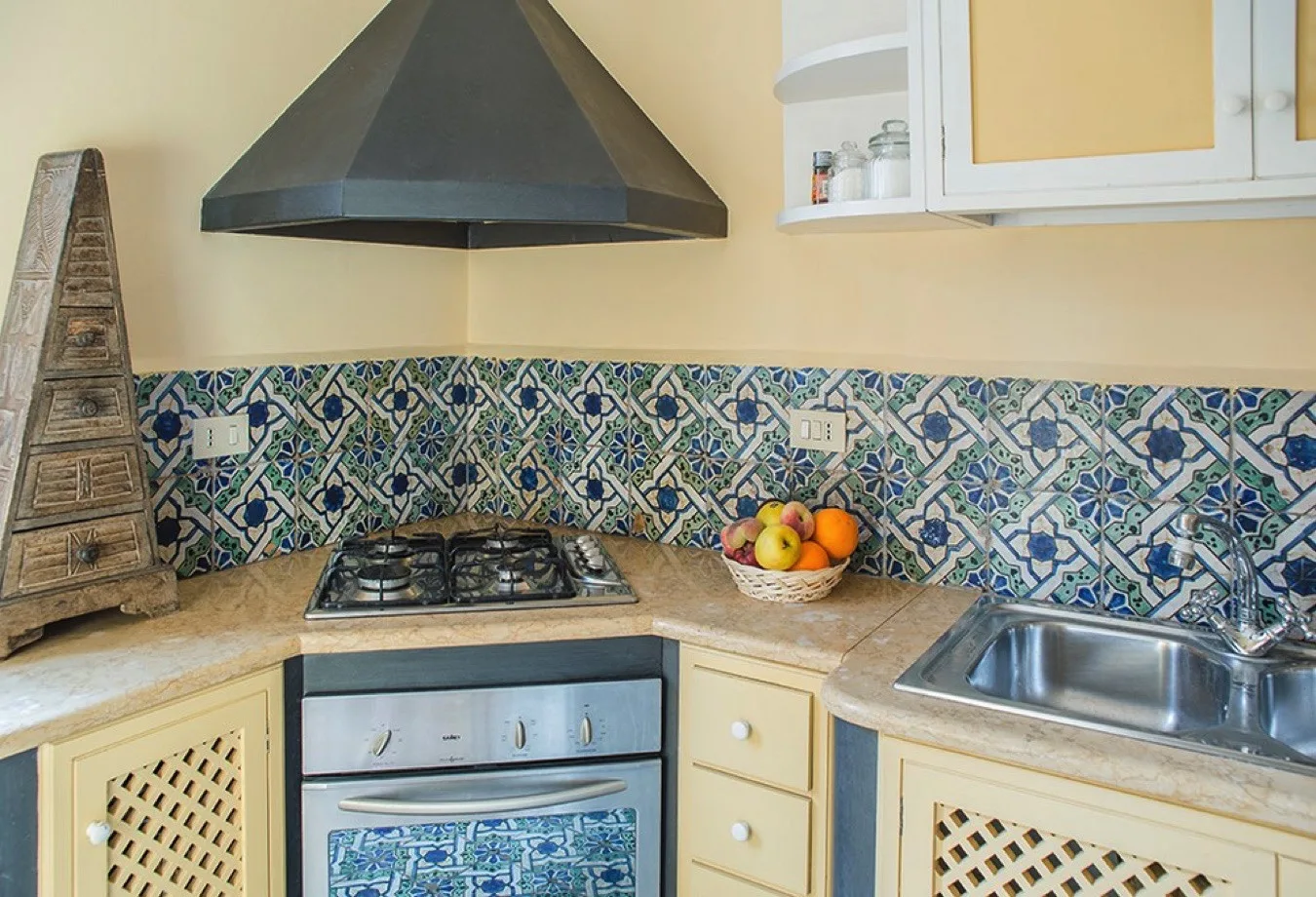 Una esquina de cocina con una placa de gas, un fregadero y azulejos decorados.
