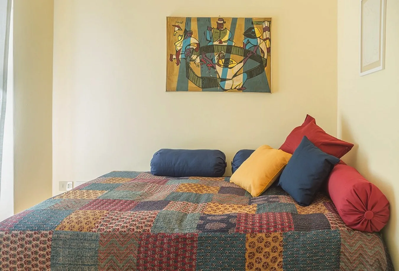 Un dormitorio con una colcha de retazos colorida y almohadas bajo una pintura enmarcada.
