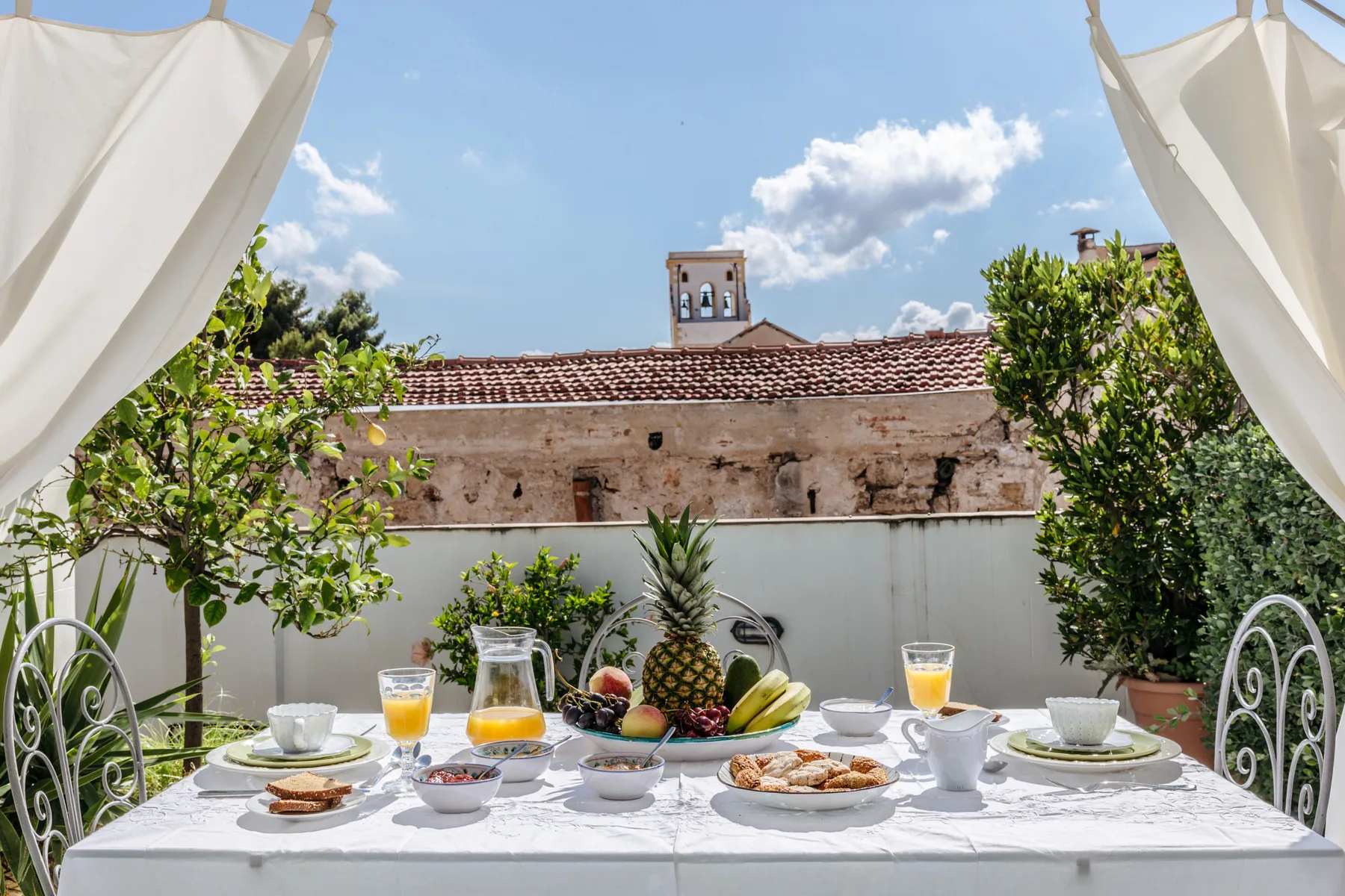 Una mesa de desayuno está preparada al aire libre con fruta bajo un cielo azul.