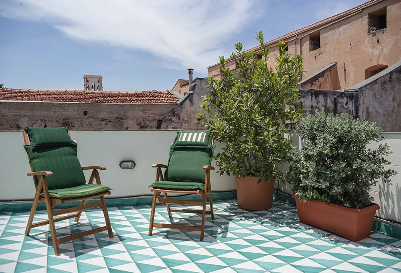 Una terraza en la azotea con asientos verdes y plantas en macetas sobre un suelo de baldosas estampadas.