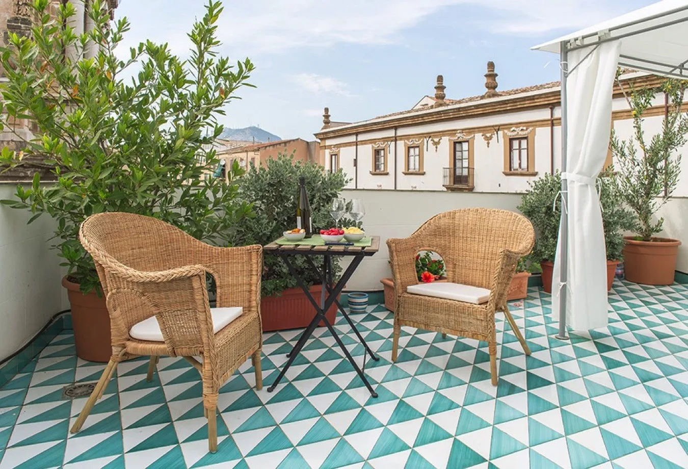 Una terraza en la azotea con asientos de mimbre, plantas en macetas y suelo de baldosas estampadas.