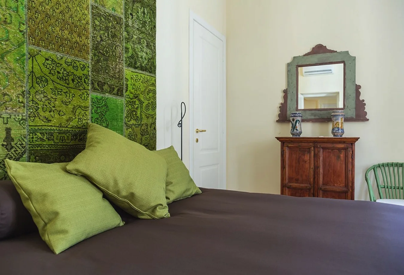 Un dormitorio con ropa de cama oscura y almohadas verdes junto a un tapiz estampado.