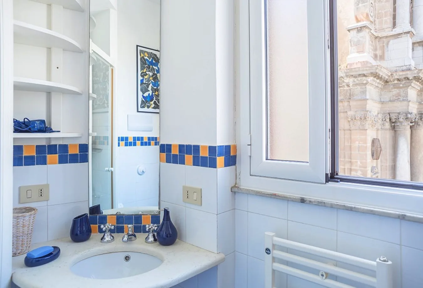 Un lavabo de baño está junto a una ventana con vistas a un edificio ornamentado.