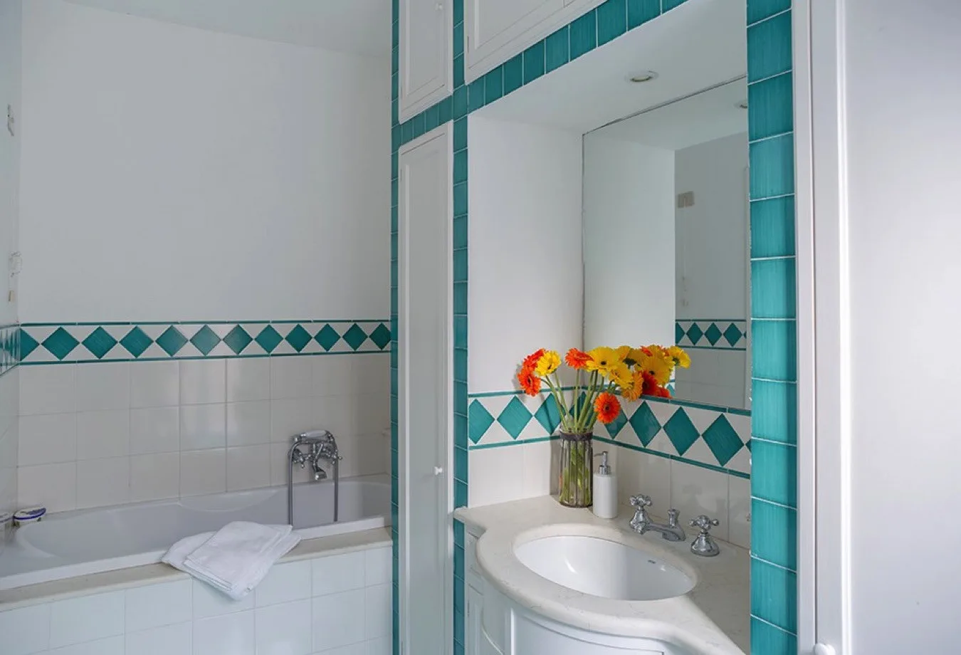 Un baño alicatado con bañera, lavabo y flores junto al espejo.