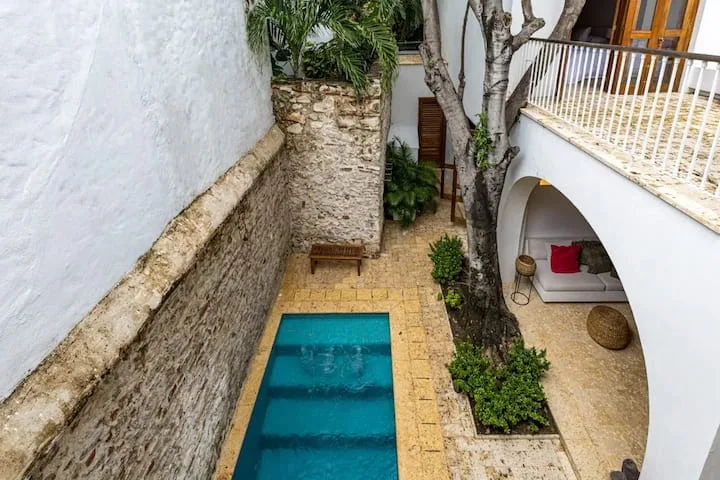 Una pequeña piscina de patio está junto a muros de piedra y una zona de estar sombreada.