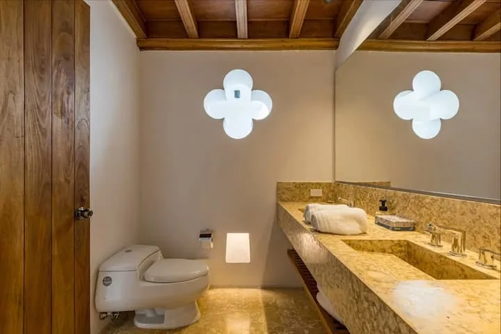 Un baño con un inodoro y un largo tocador de piedra bajo vigas de madera expuestas.