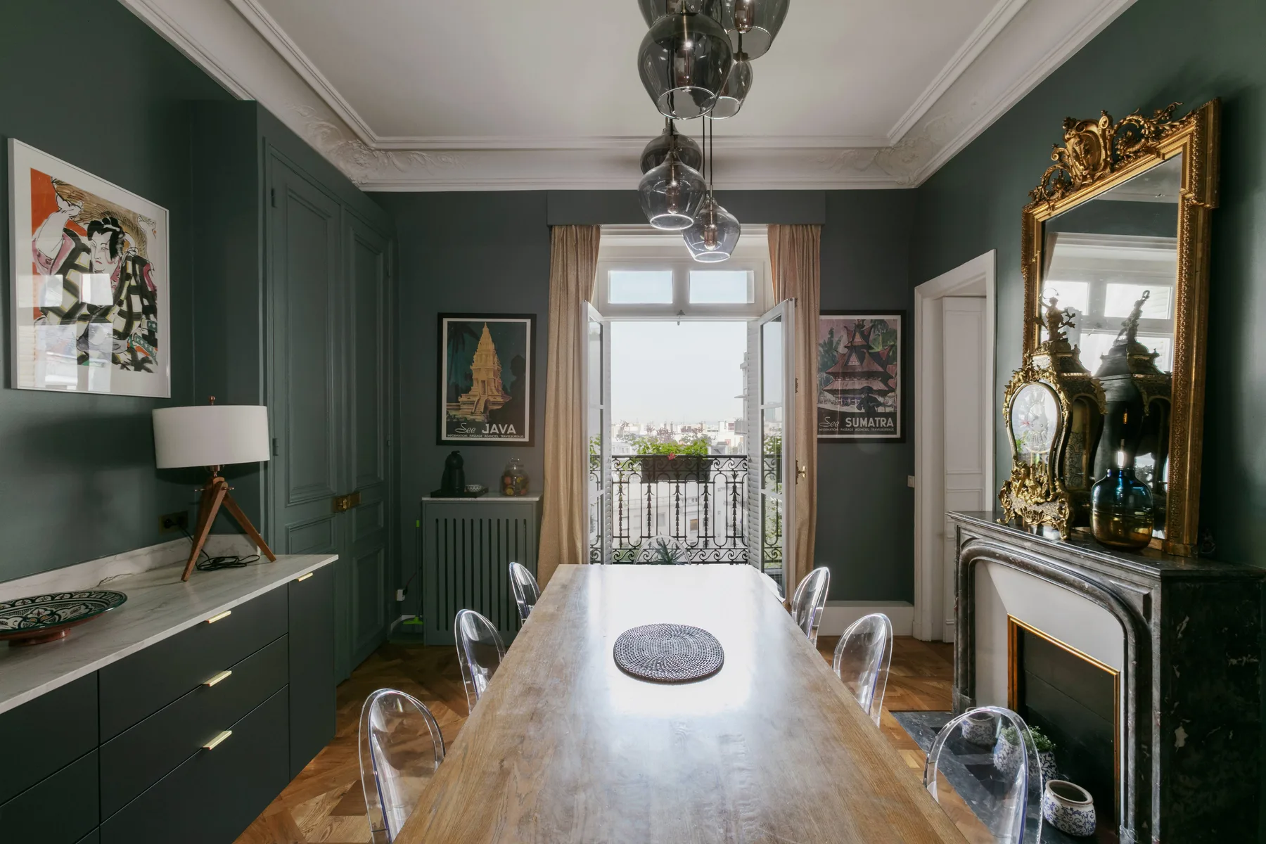 Comedor con una mesa larga, lámparas colgantes y paredes verde oscuro.