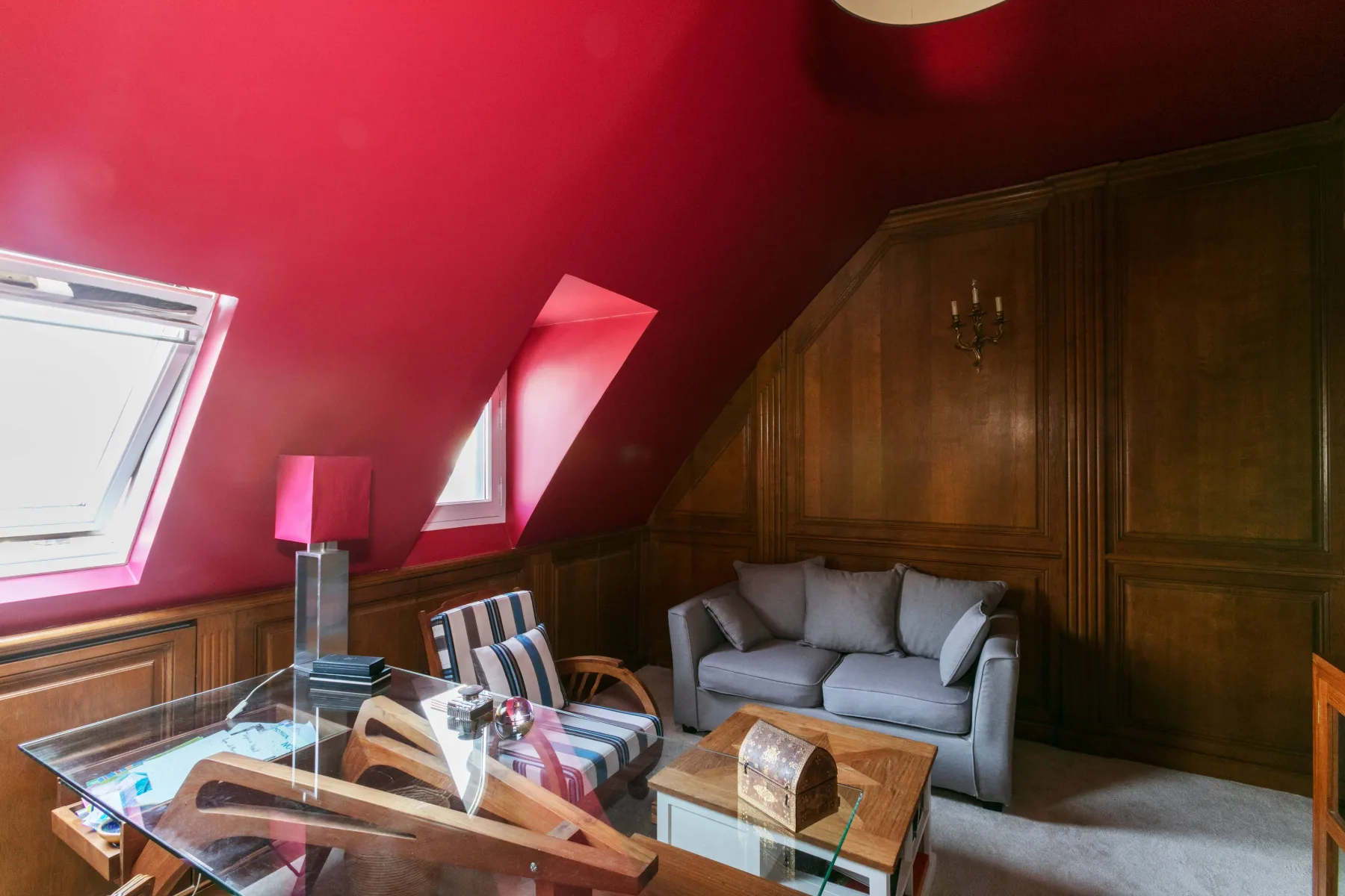Una sala de estar con un sofá gris y una mesa de centro de vidrio bajo un techo rojo inclinado.