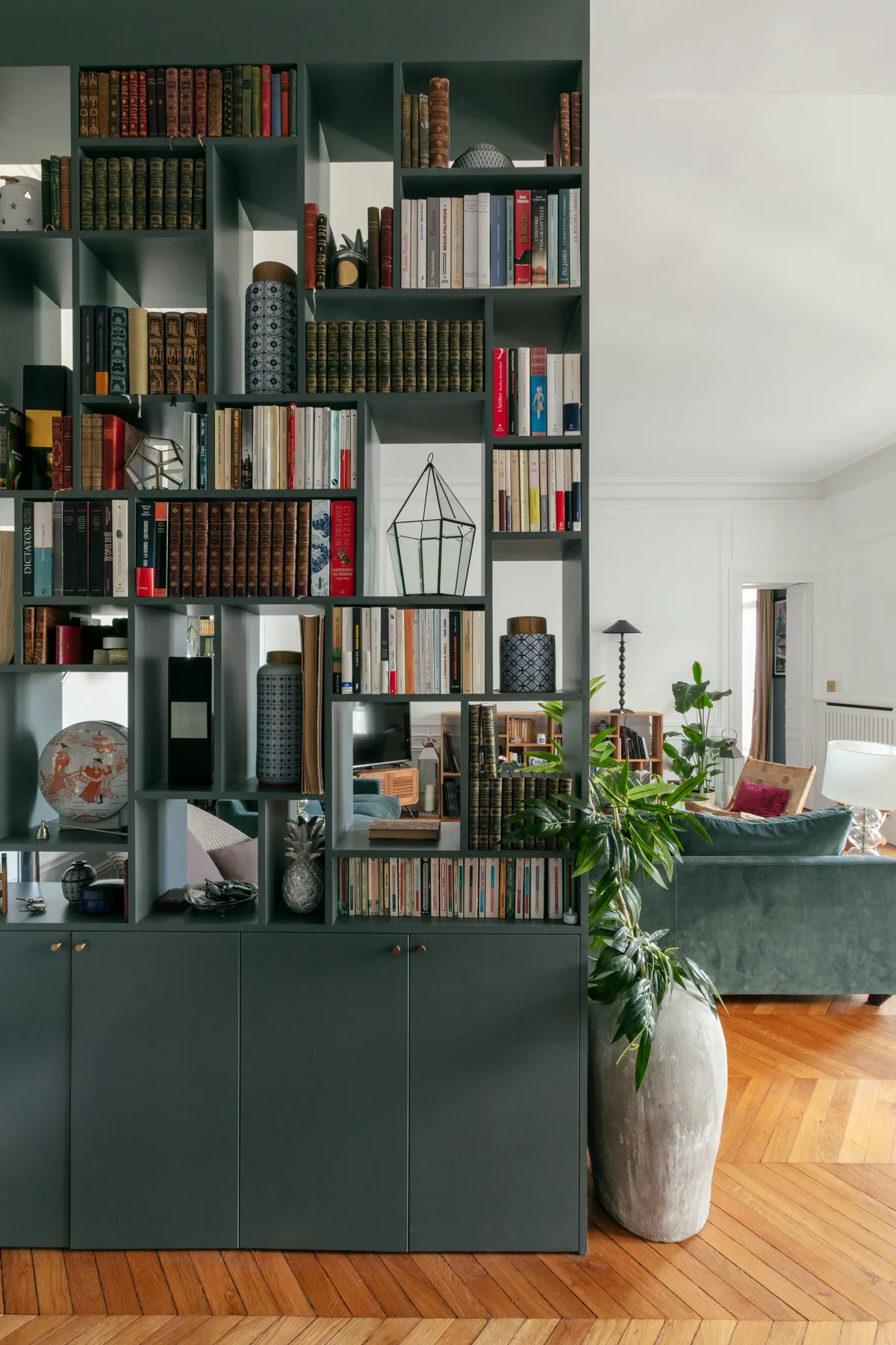 Una estantería alta llena de libros y objetos decorativos está junto a una sala de estar.