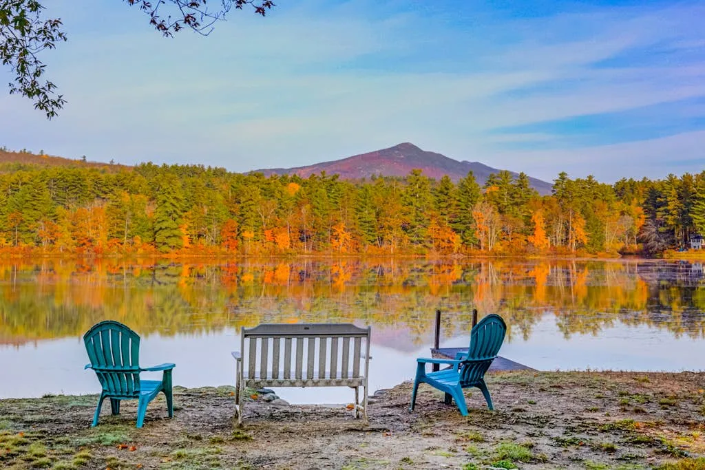 Outdoor seating faces a calm lake with autumn-colored trees and a mountain beyond.