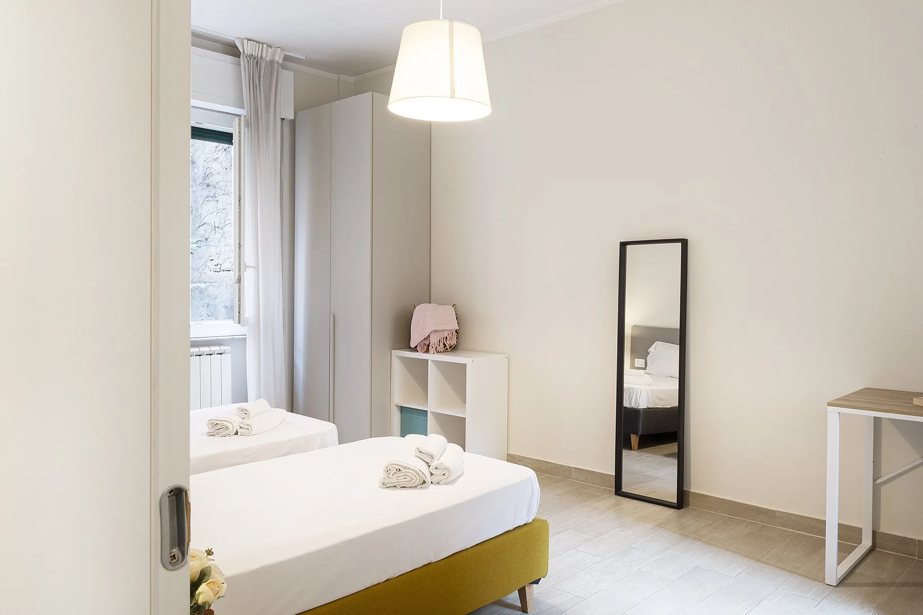 A bedroom with a neatly made bed and a full-length mirror.
