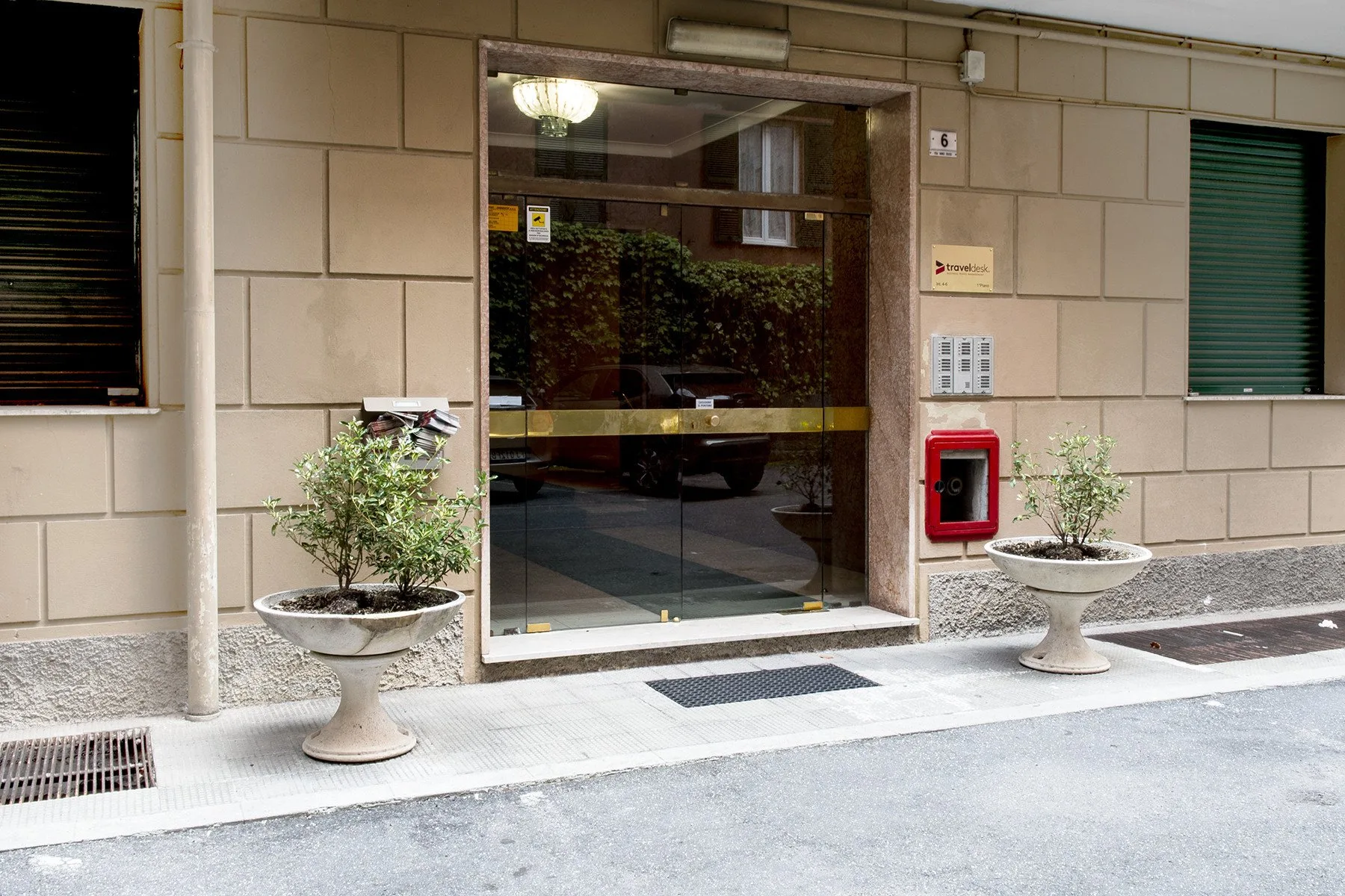 A building entrance with a glass door and potted plants on either side.