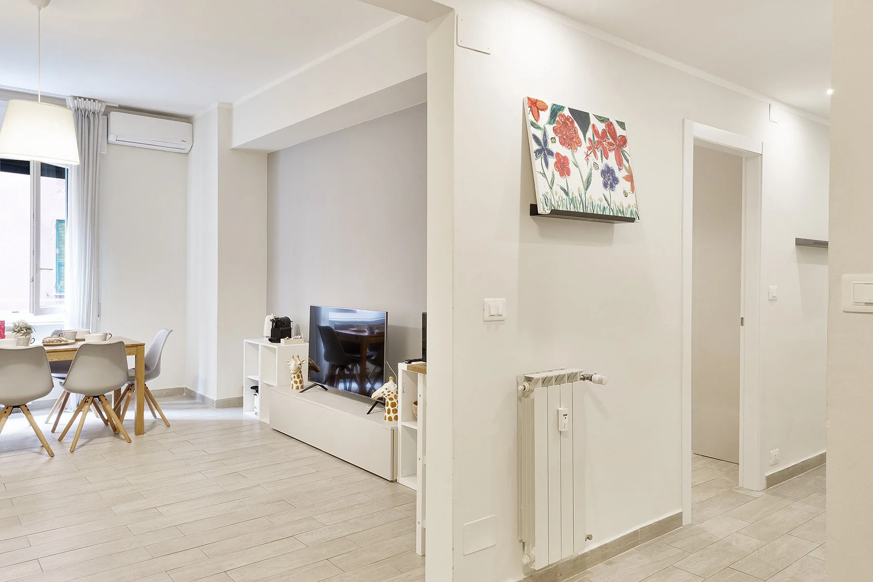 A bright living and dining area with seating, a television, and a wall-mounted air conditioner.