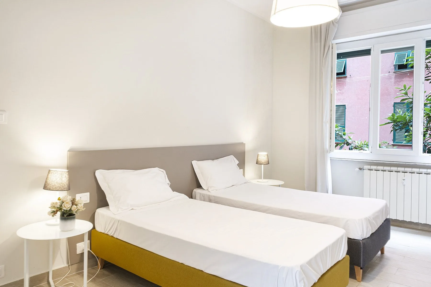 A bright bedroom with two beds beside a large window.