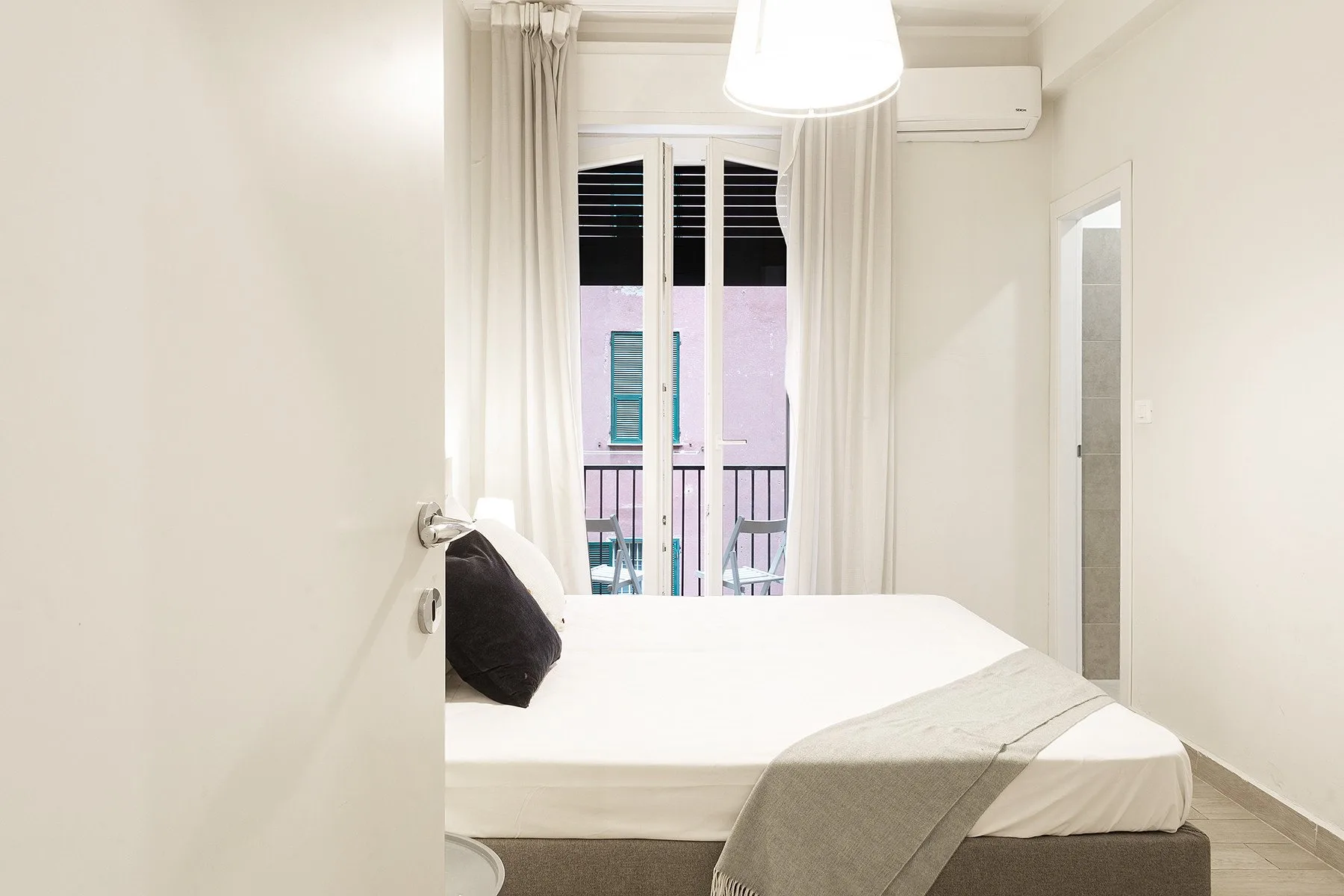 A bright bedroom with a neatly made bed and curtains beside the balcony doors.