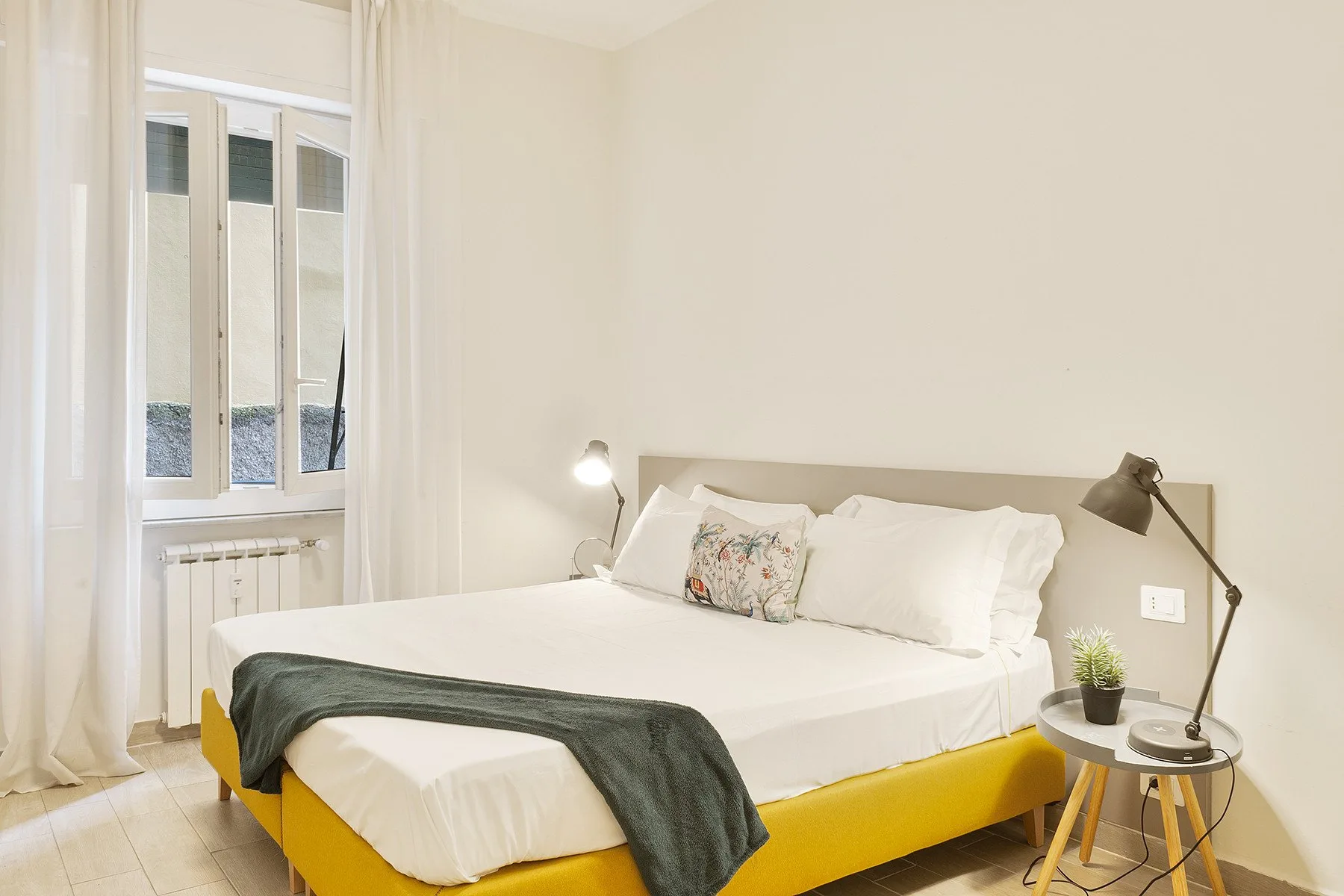 A bedroom with a bed, bedside lamps, and a window with curtains.