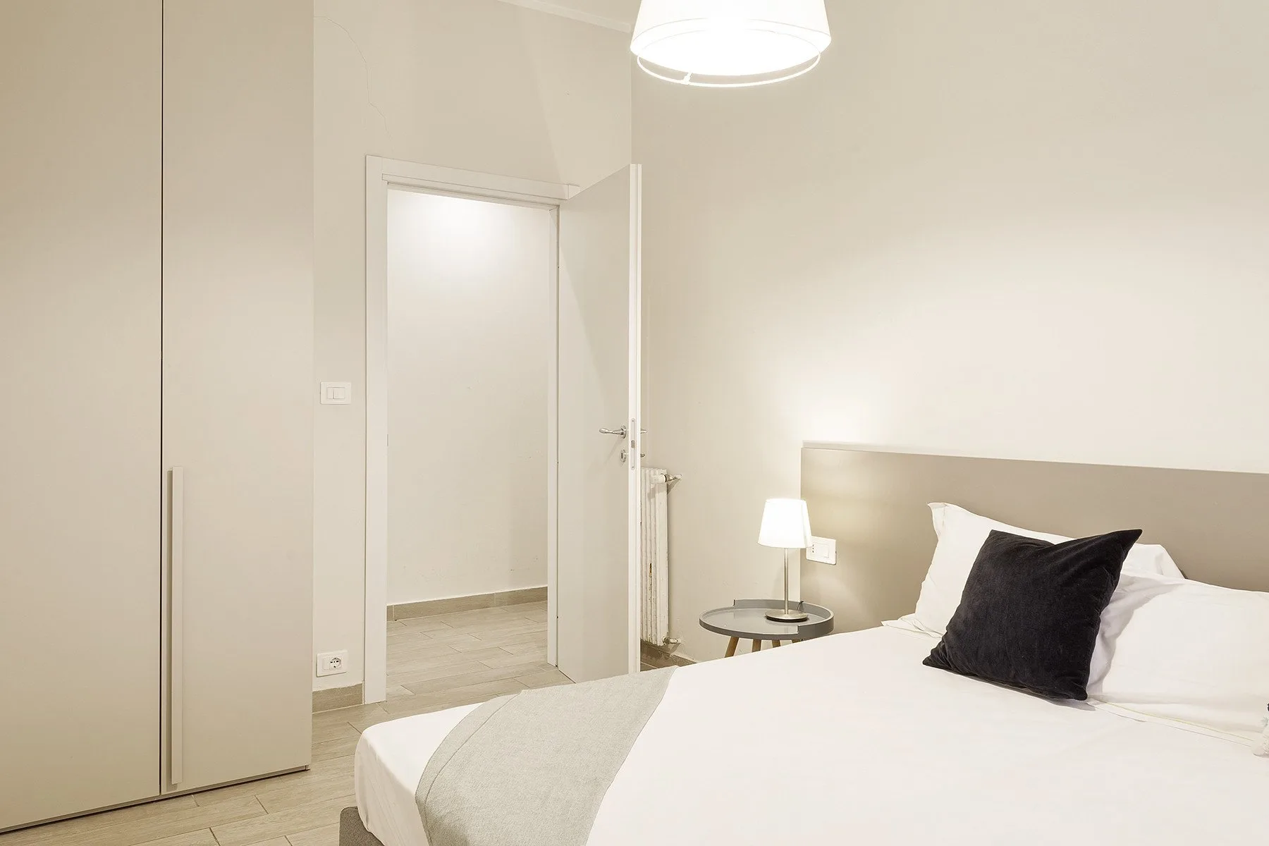 A bright bedroom with a neatly made bed and bedside lamp.