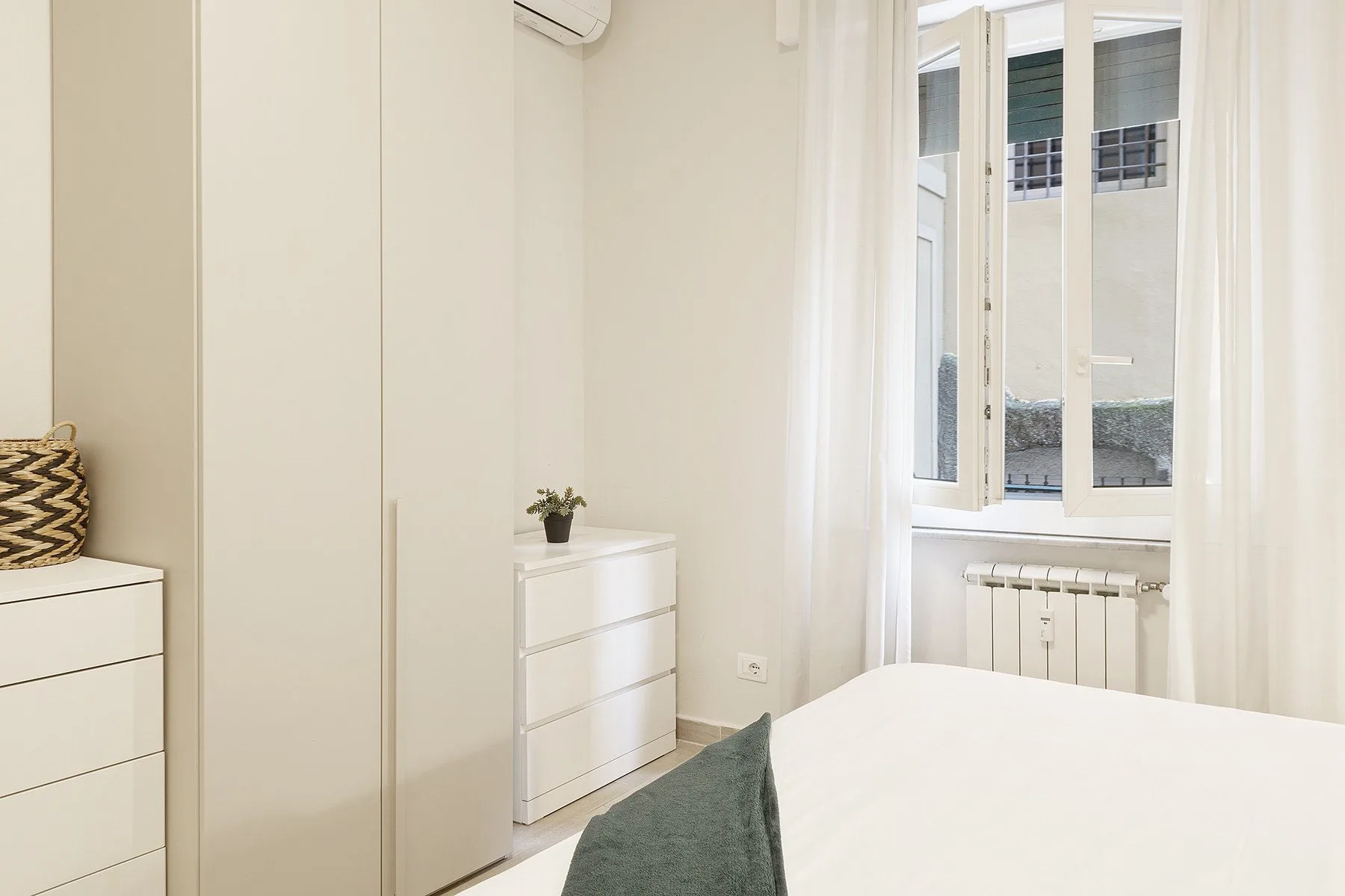 A bright bedroom with a bed, white dressers, and a window.