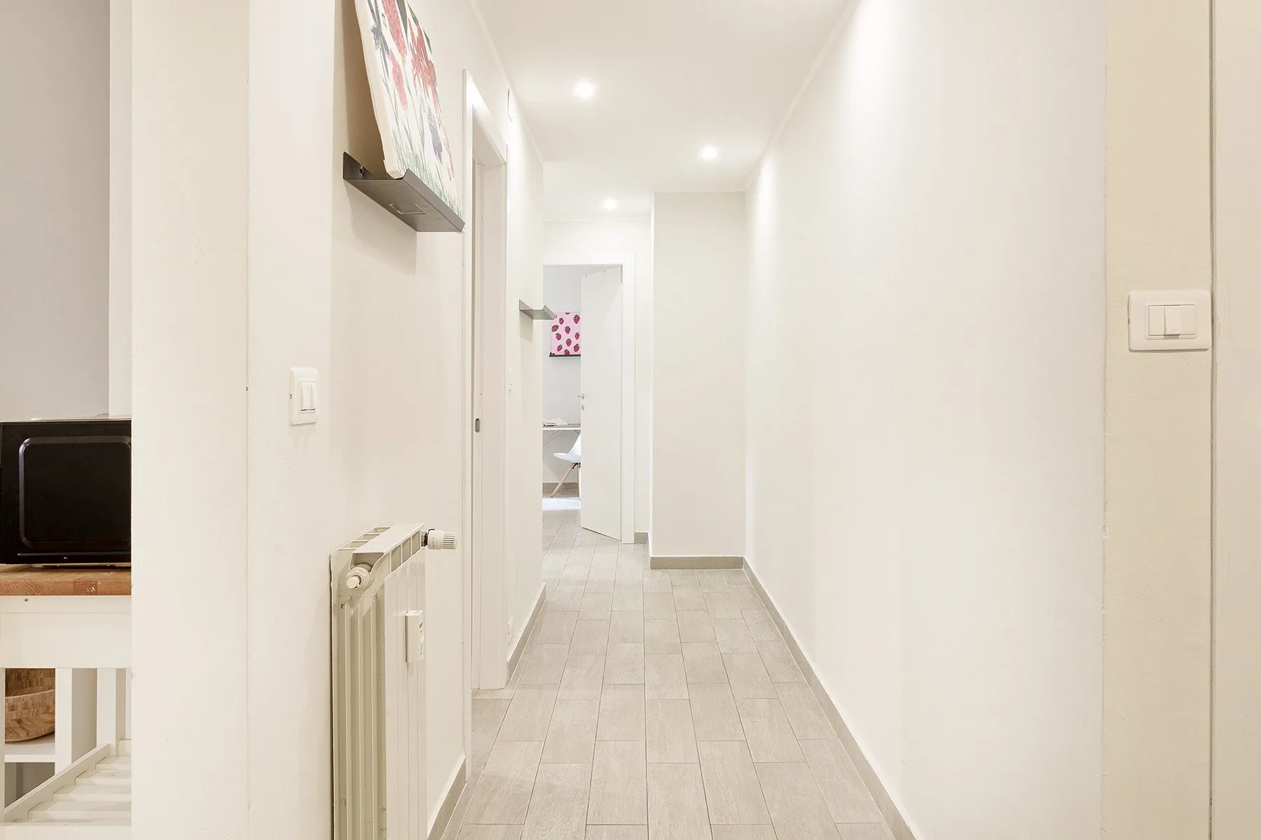 A bright hallway with light tile flooring and open doorways.
