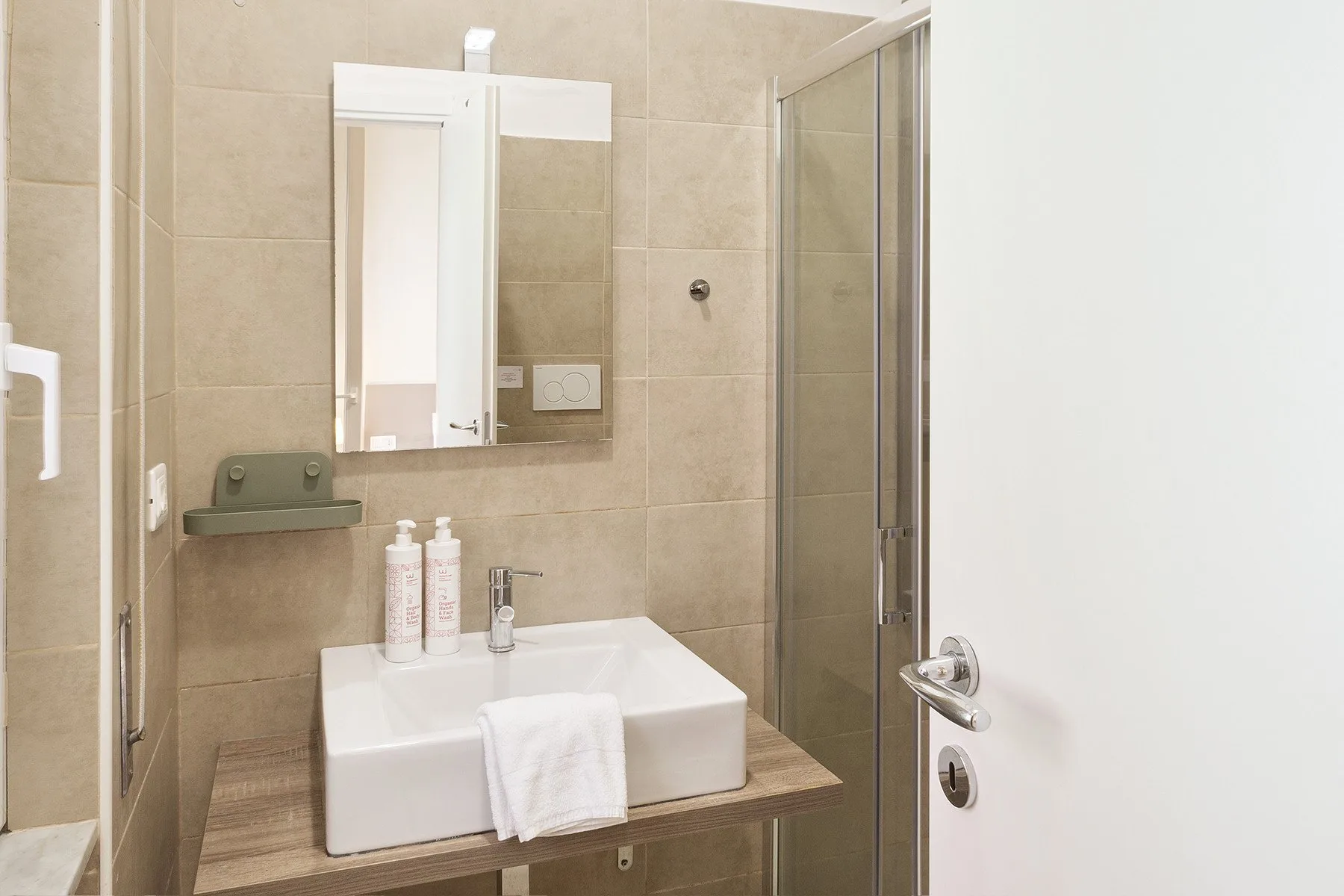 A tiled bathroom with a basin, mirror, and glass shower.
