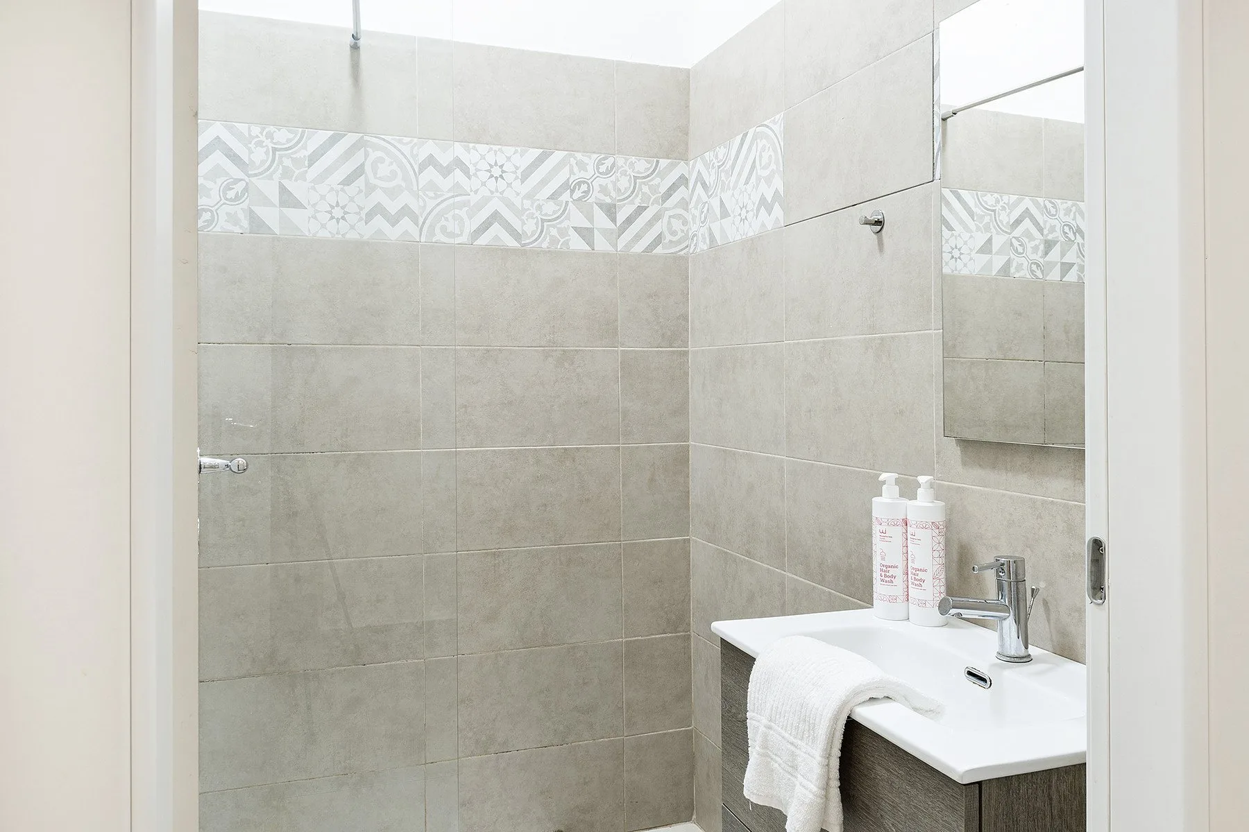 A tiled bathroom with a shower and a sink beneath a wall mirror.