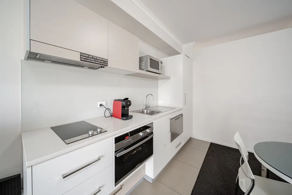 Una cocina blanca compacta con placa de cocción, horno y fregadero.
