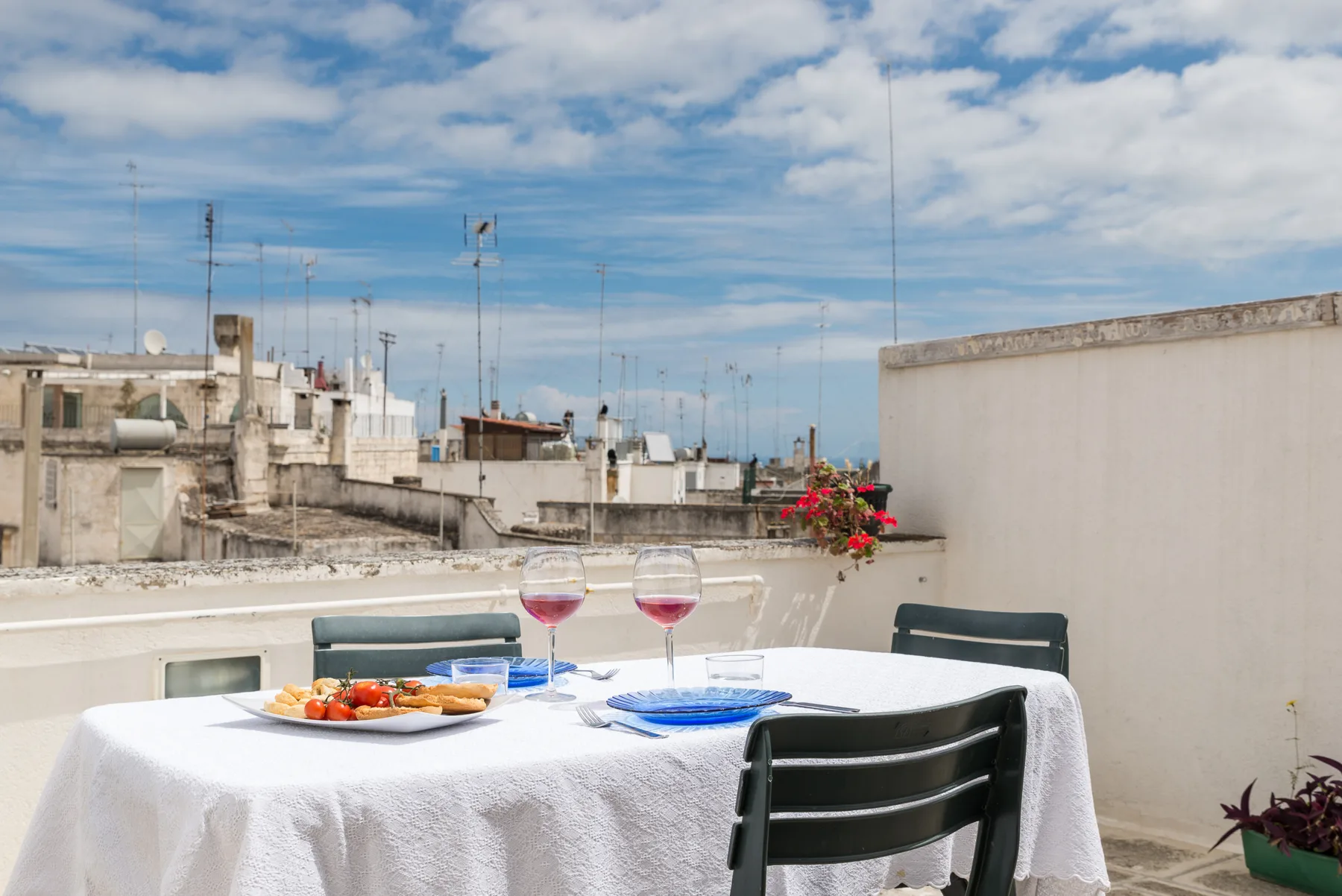 Una mesa de comedor en una terraza tiene platos y copas bajo un cielo parcialmente nublado.