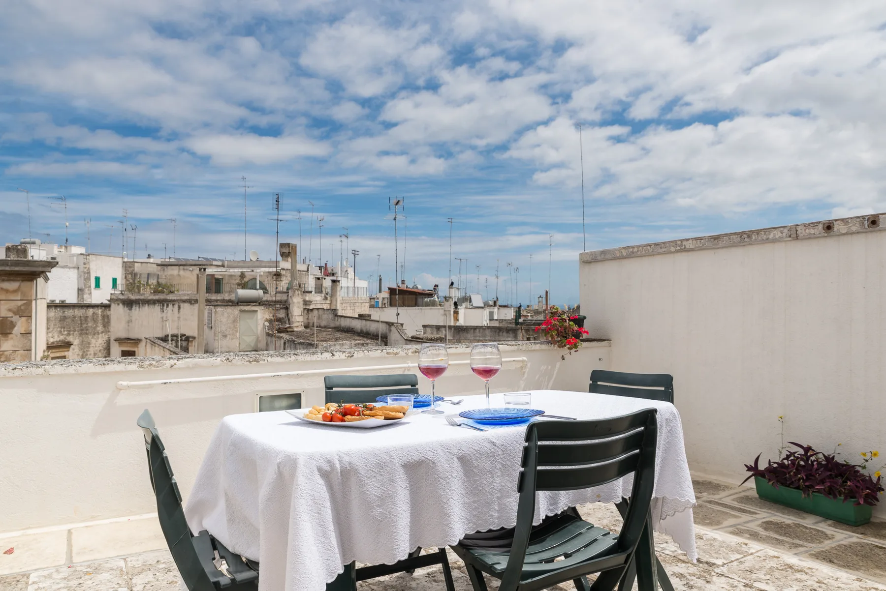 Una zona de comedor en la azotea tiene una mesa puesta con platos y copas bajo un cielo nublado.
