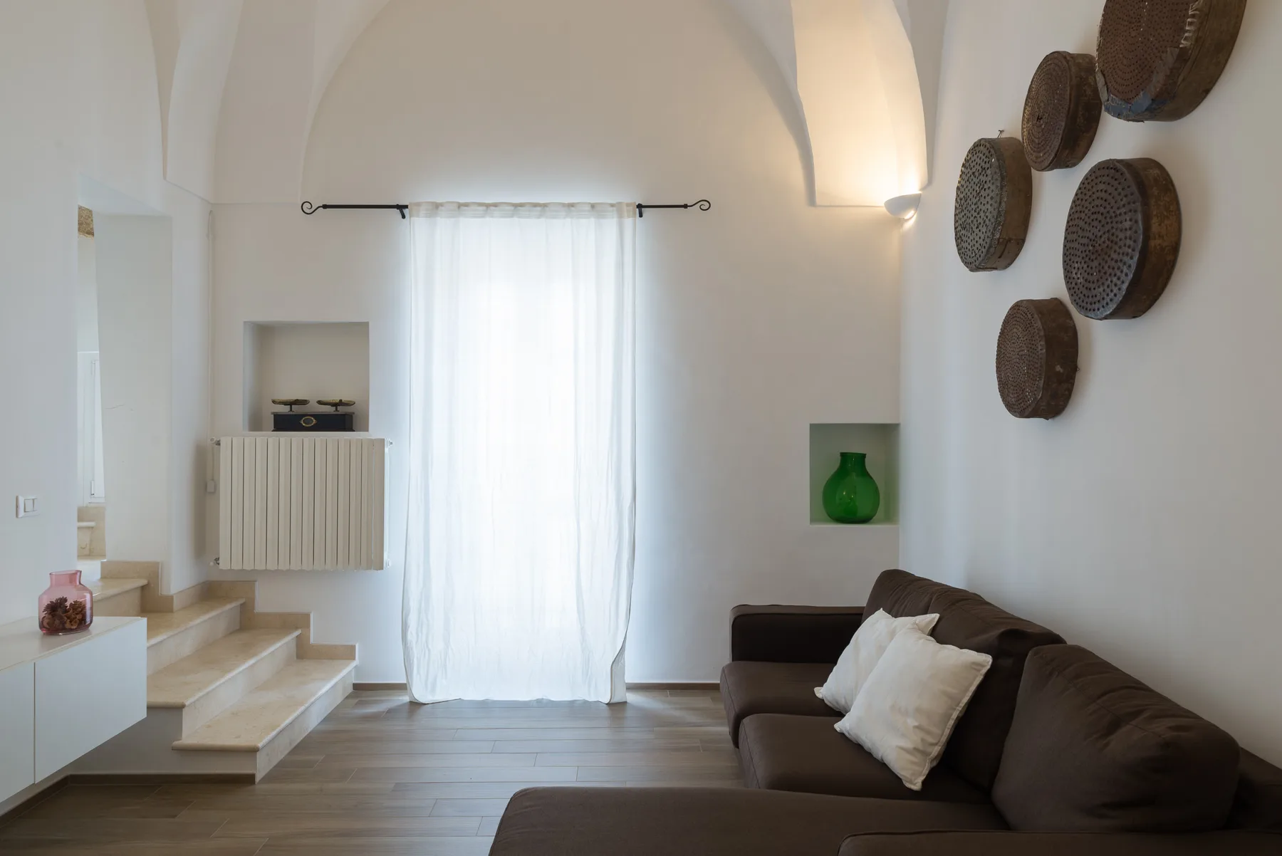 Una sala luminosa con un sofá marrón, cortinas translúcidas y escalones.