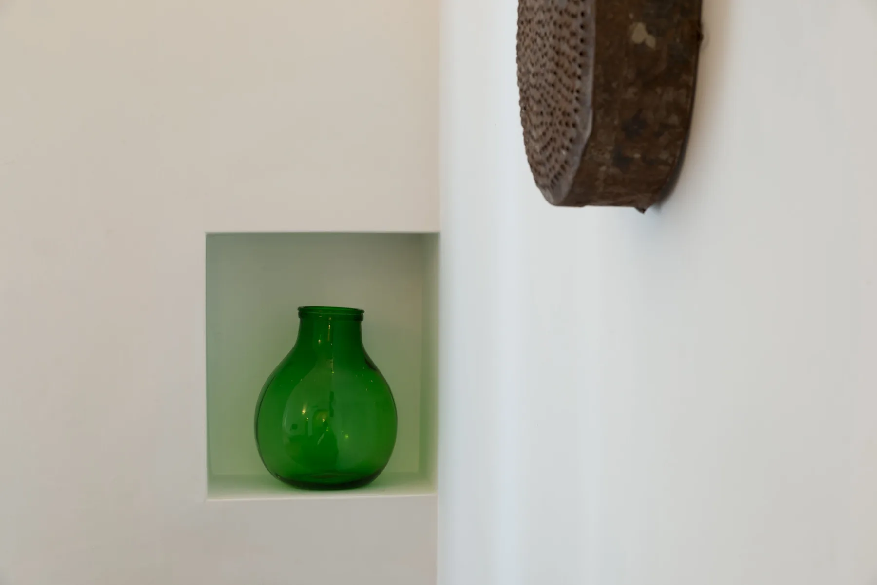 Un jarrón de vidrio verde está en un nicho de pared junto a una pieza decorativa.