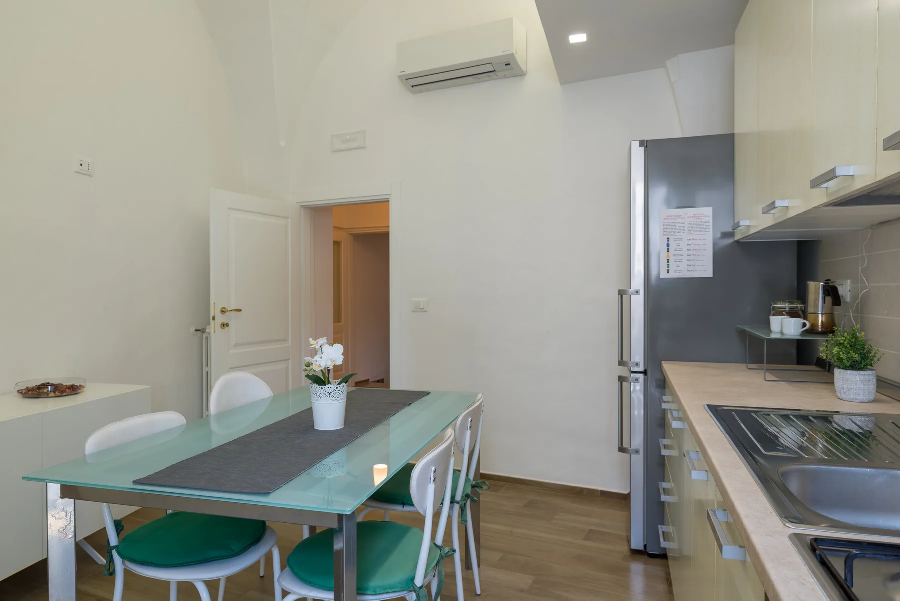 Una cocina y comedor luminosos con una mesa de vidrio y electrodomésticos integrados.