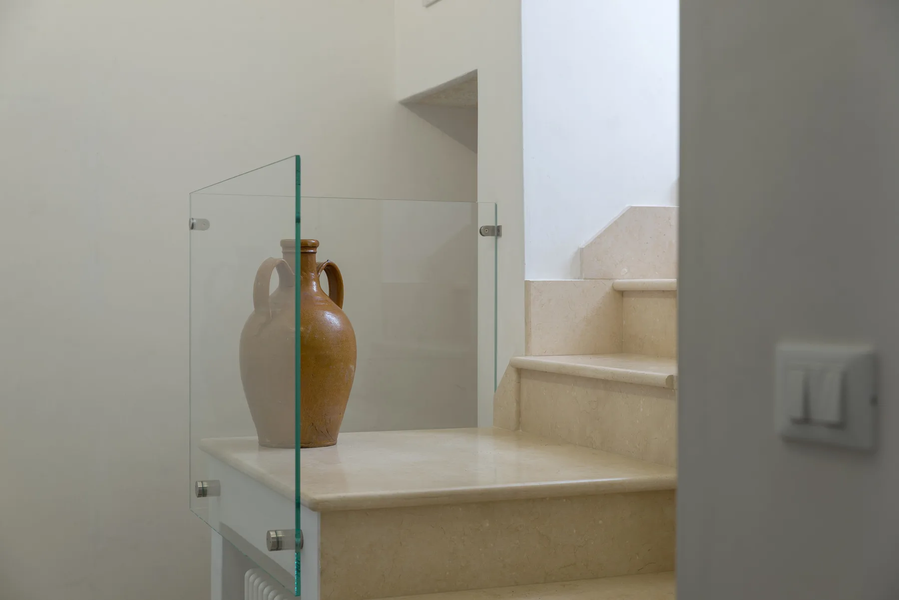 Una escalera con barandilla de vidrio y un jarrón decorativo de cerámica.