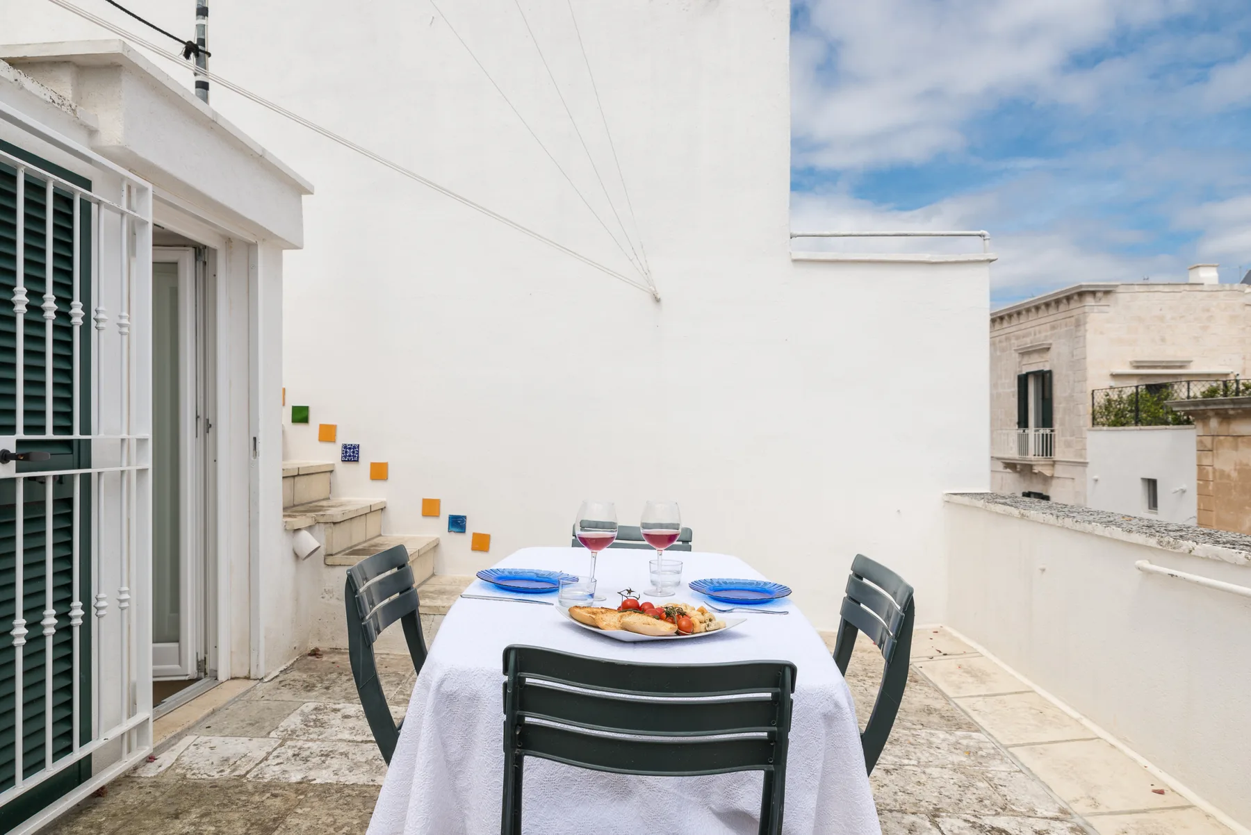 Una zona de comedor en la azotea con una mesa preparada junto a una pared blanca.