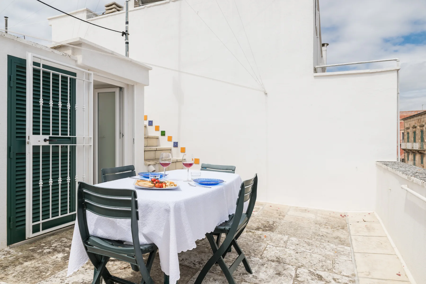 Un comedor al aire libre con una mesa puesta junto a una pared blanca.