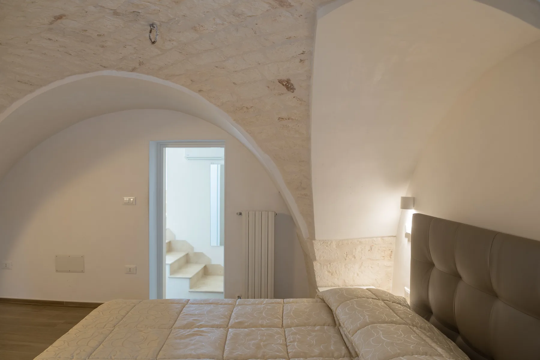 Un dormitorio con una cama bajo un techo curvo y una puerta abierta.