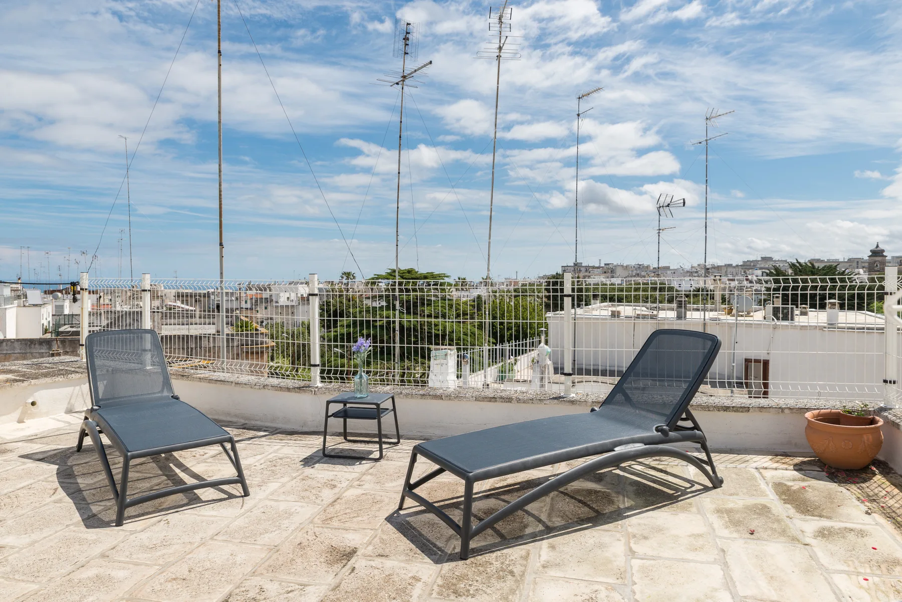 Una terraza en la azotea tiene dos tumbonas reclinables, una mesa pequeña y vistas de la ciudad.